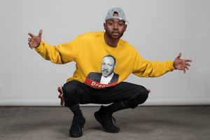 Black man with backwards baseball hat wearing a gold mens unisex Martin Luther King Junior Dream sweatshirt